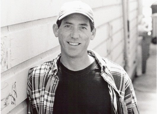 Black and white photo of Tommy Angelo smiling at the camera 