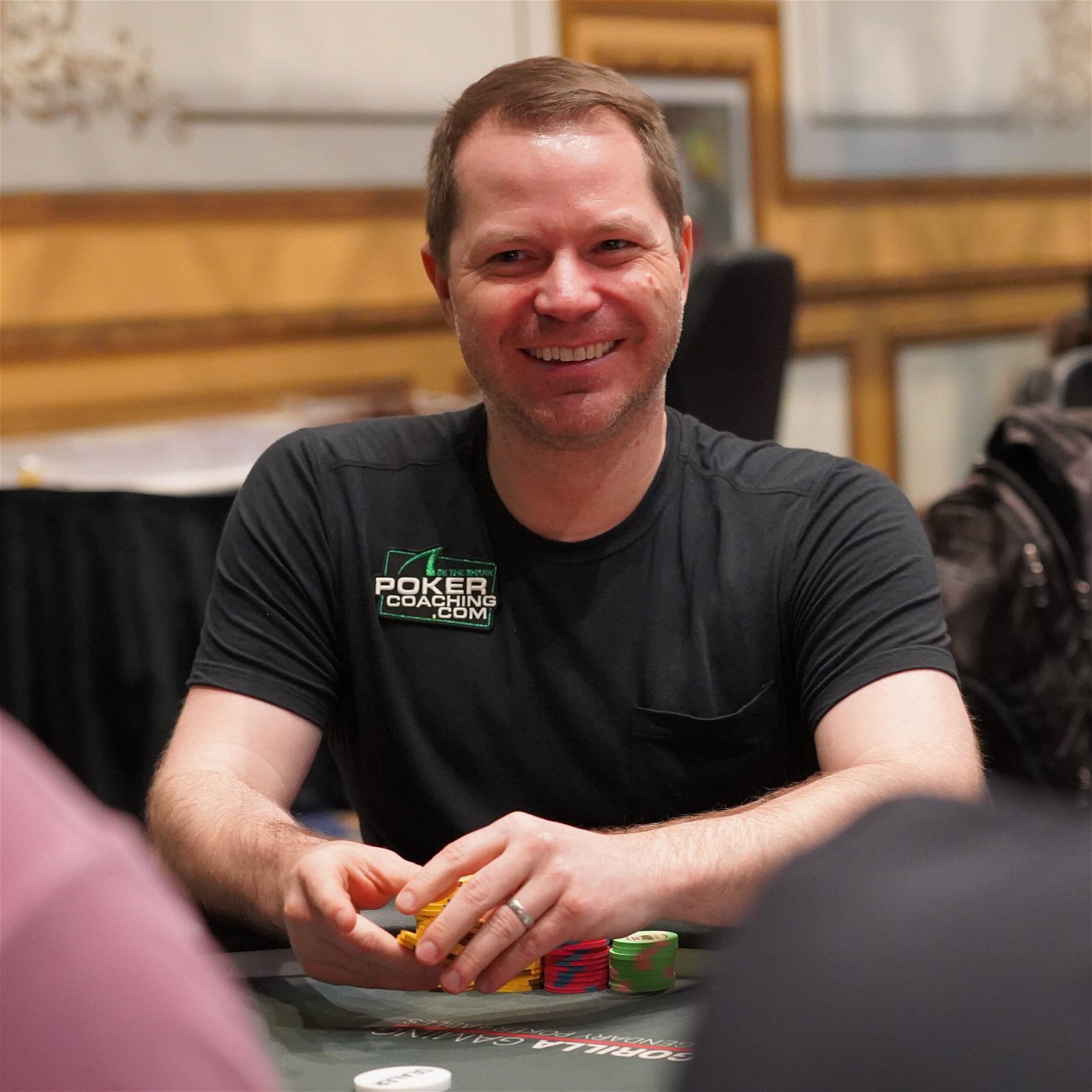 Jonathan Little smiling and wearing a PokerCoaching.com patch at the poker table